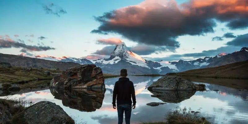 man facing mountain lake, storm clouds gathering in sky