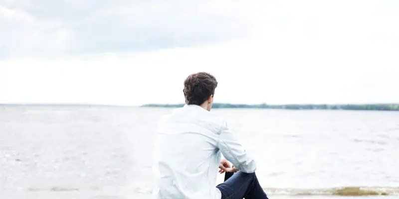 young man seated on shore facing out toward the water