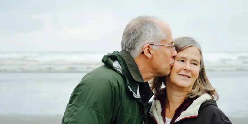 older man in green jacket kissing woman on the cheek