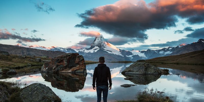 man standing at water's edge gazing at mountain in the distance