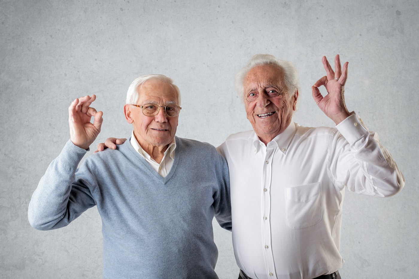 two elderly men side by side making the OK sign